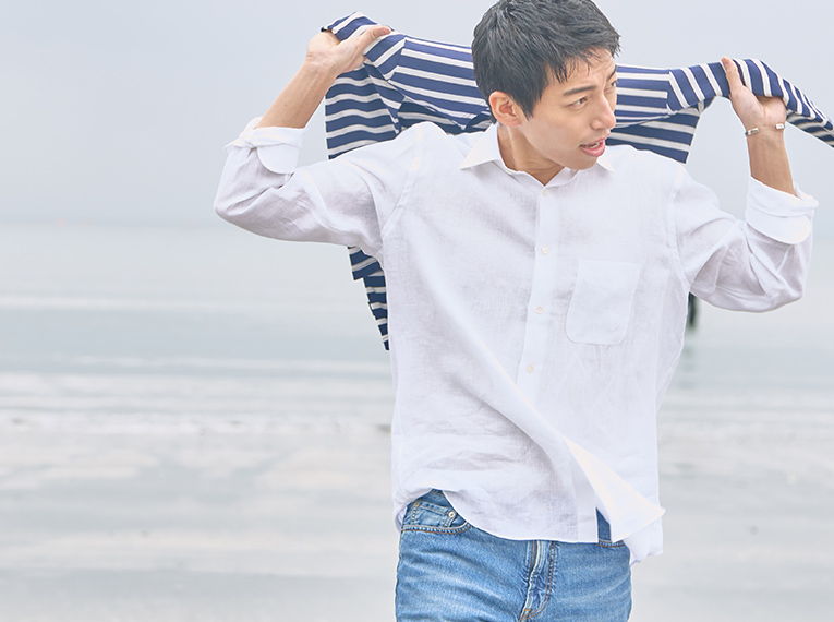 Young man in a white shirt holding a striped jacket by the sea.