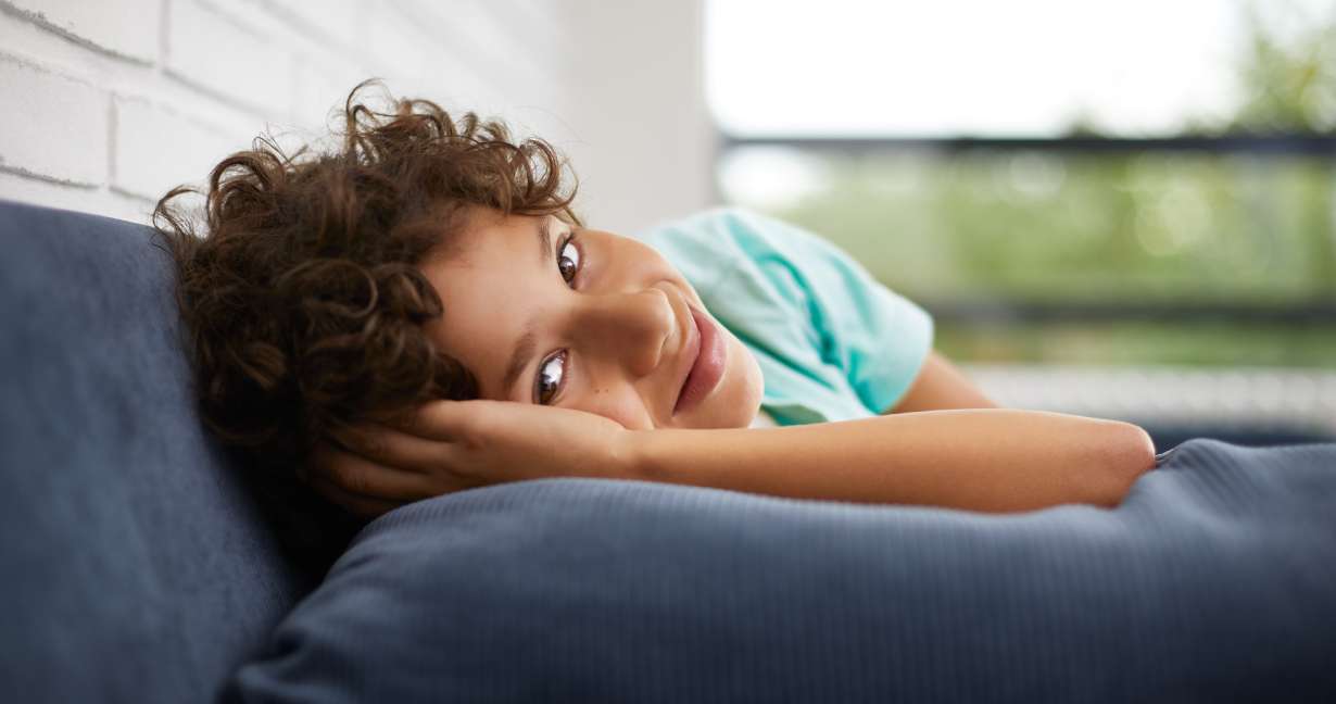 Boy lying on his sofa with his arm under his head – it’s daytime and he’s missing school again because of his allergies