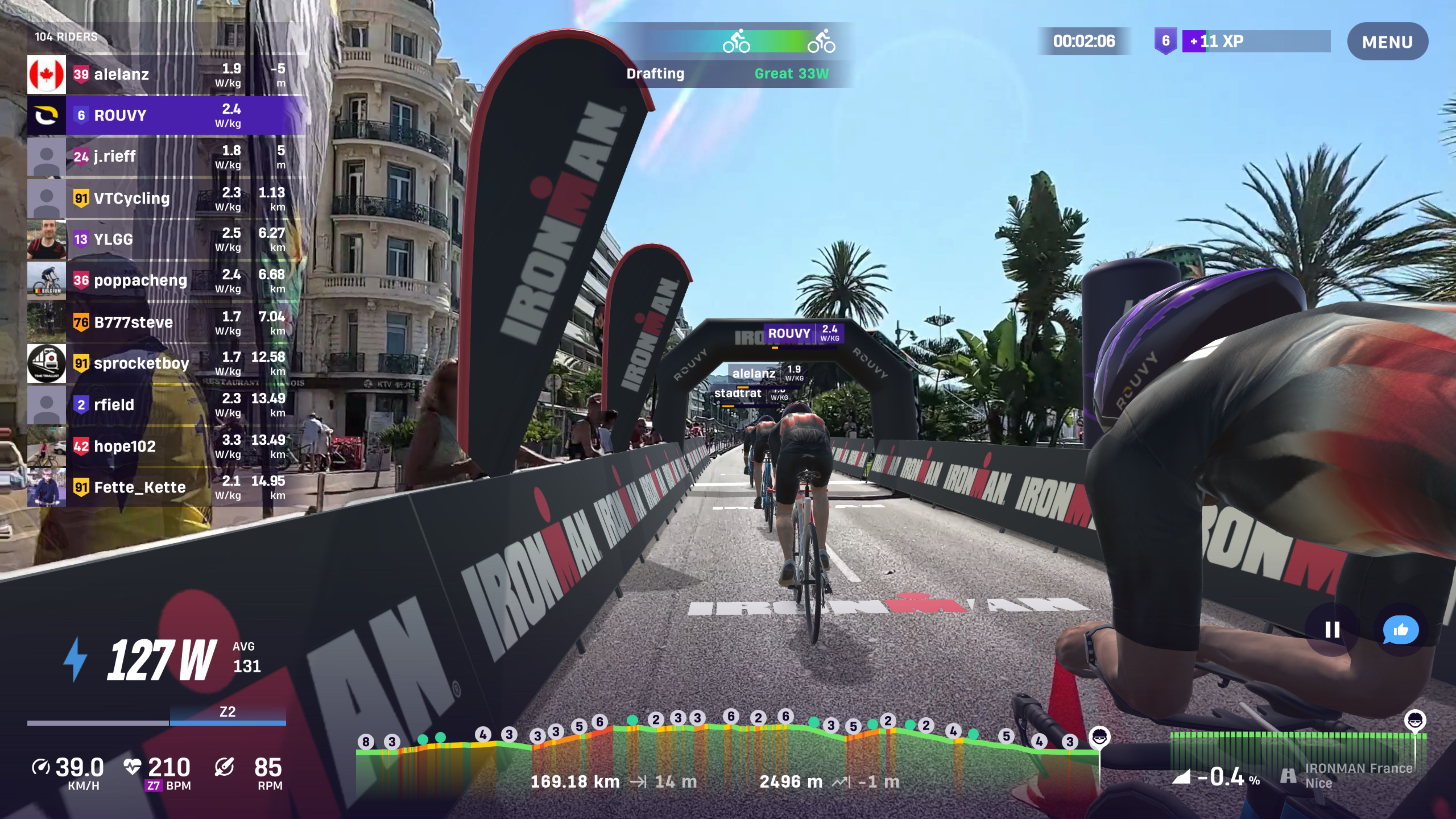 Virtuelle Radfahrer fahren in der ROUVY-App durch eine Stadtstrecke beim IRONMAN-Event, mit eingeblendeten Leistungsdaten und Rennübersicht.
