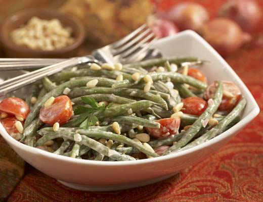 A bowl of green bean salad with tomatoes and pine nuts.