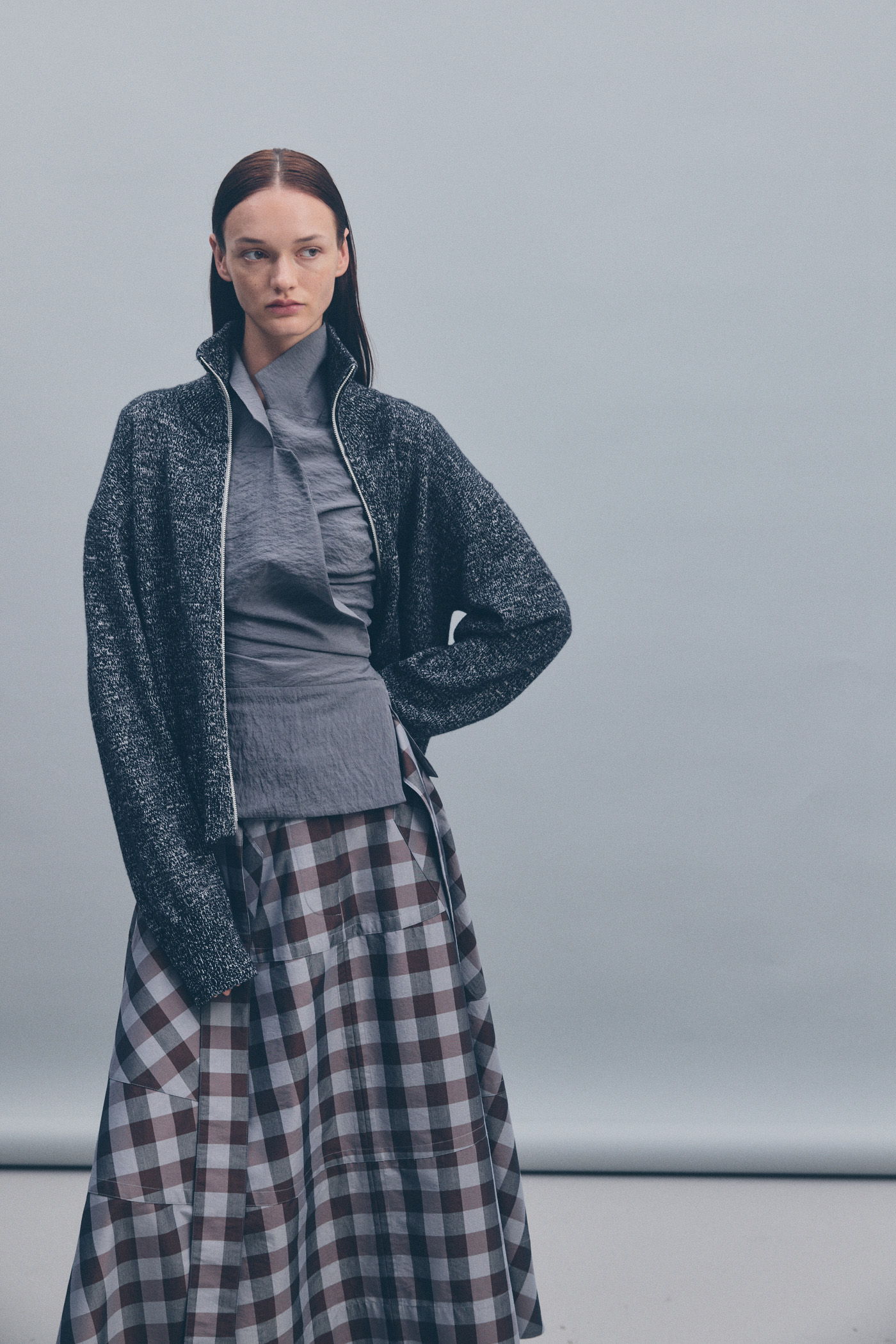 Model wearing layered clothing with a gray jacket and plaid skirt.