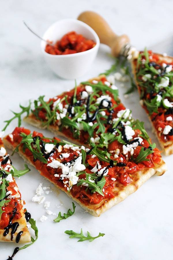 Crisp flatbread with a layer of roasted red pepper bruschetta with arugula, feta and balsamic glaze