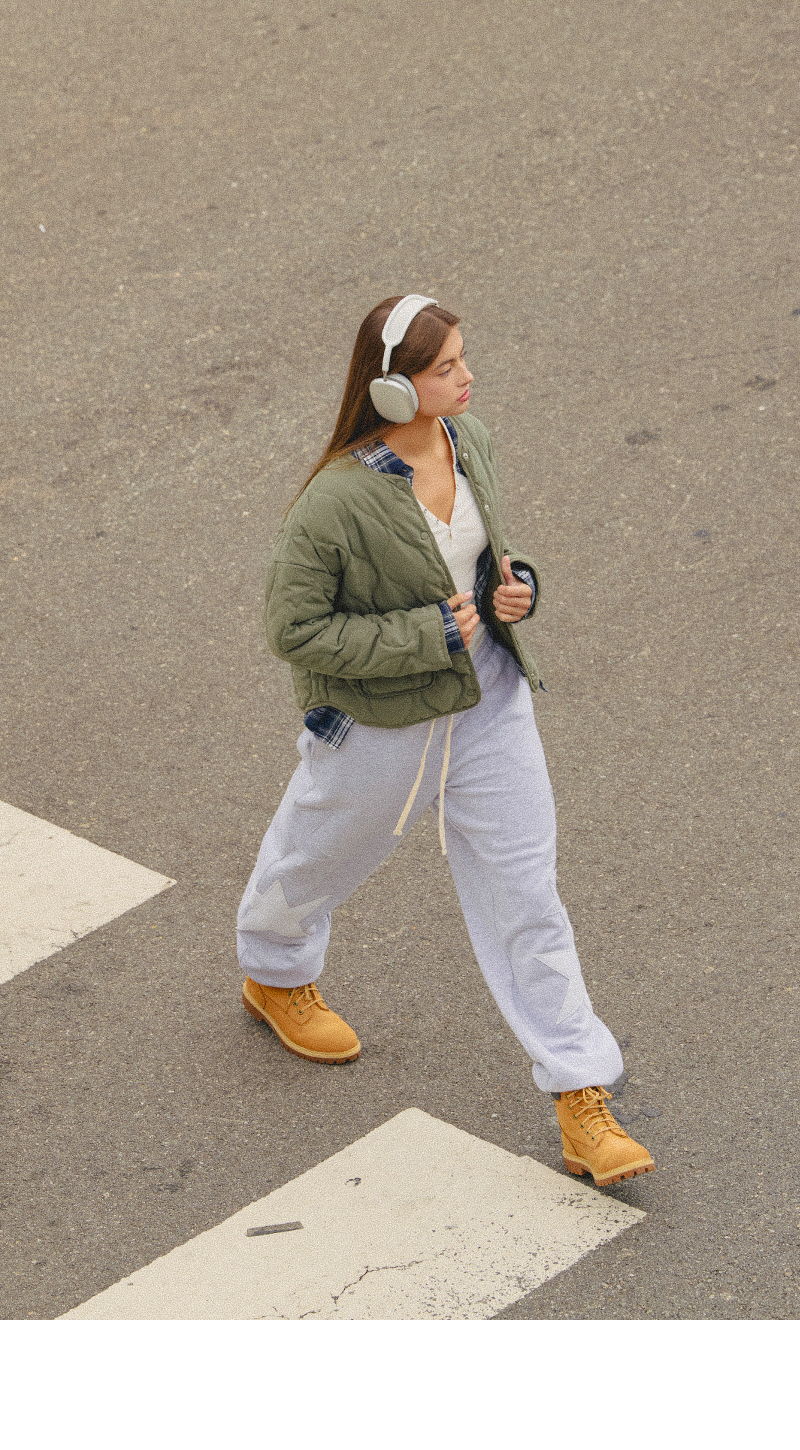 Person walking in oversized clothes and headphones across a street.
