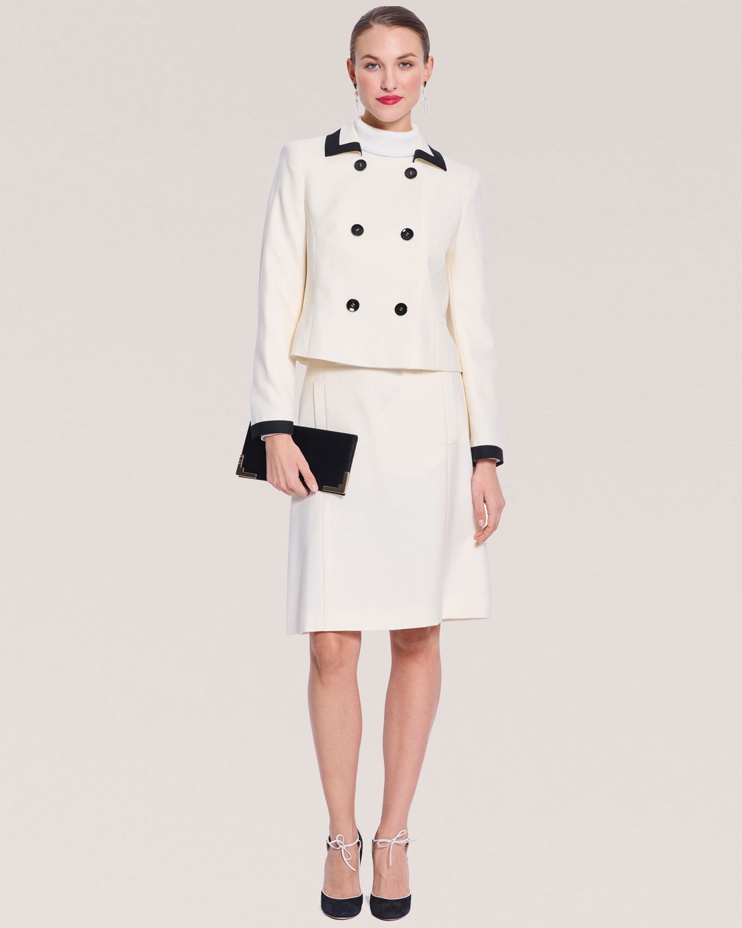 Woman in a stylish white outfit with a black clutch and heels.