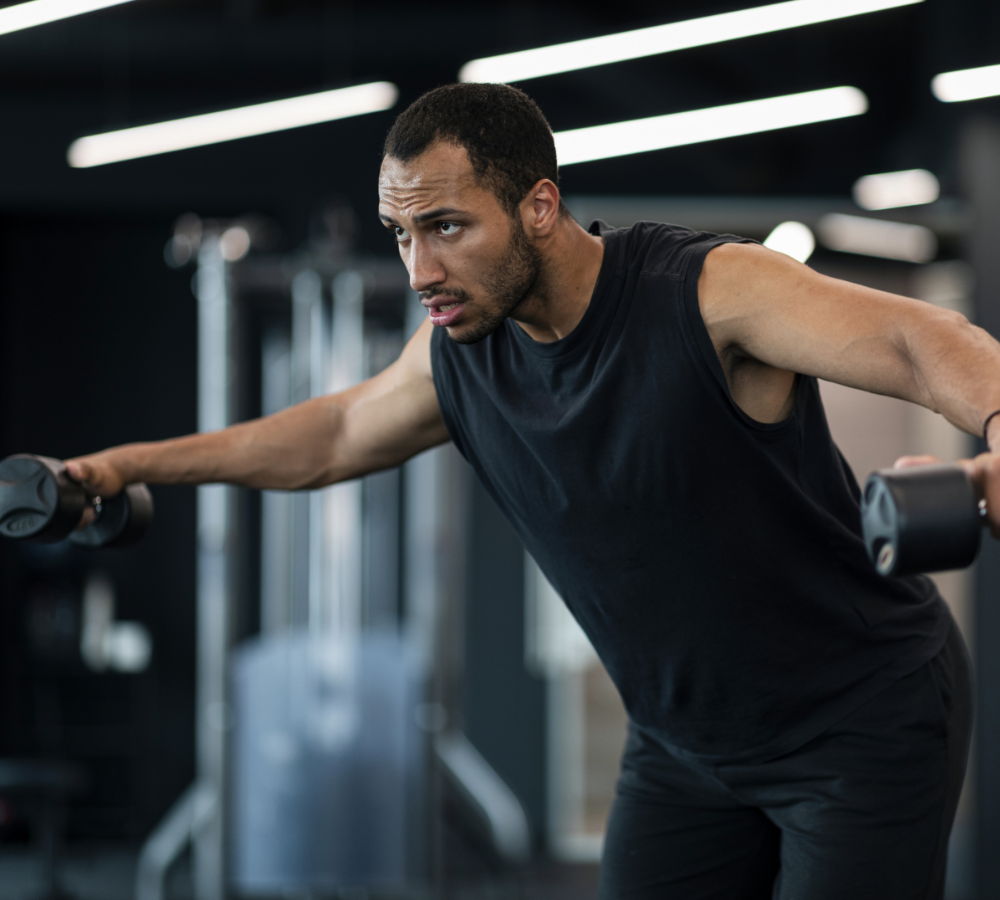 Man exercising with dumbbells in a gym setting.