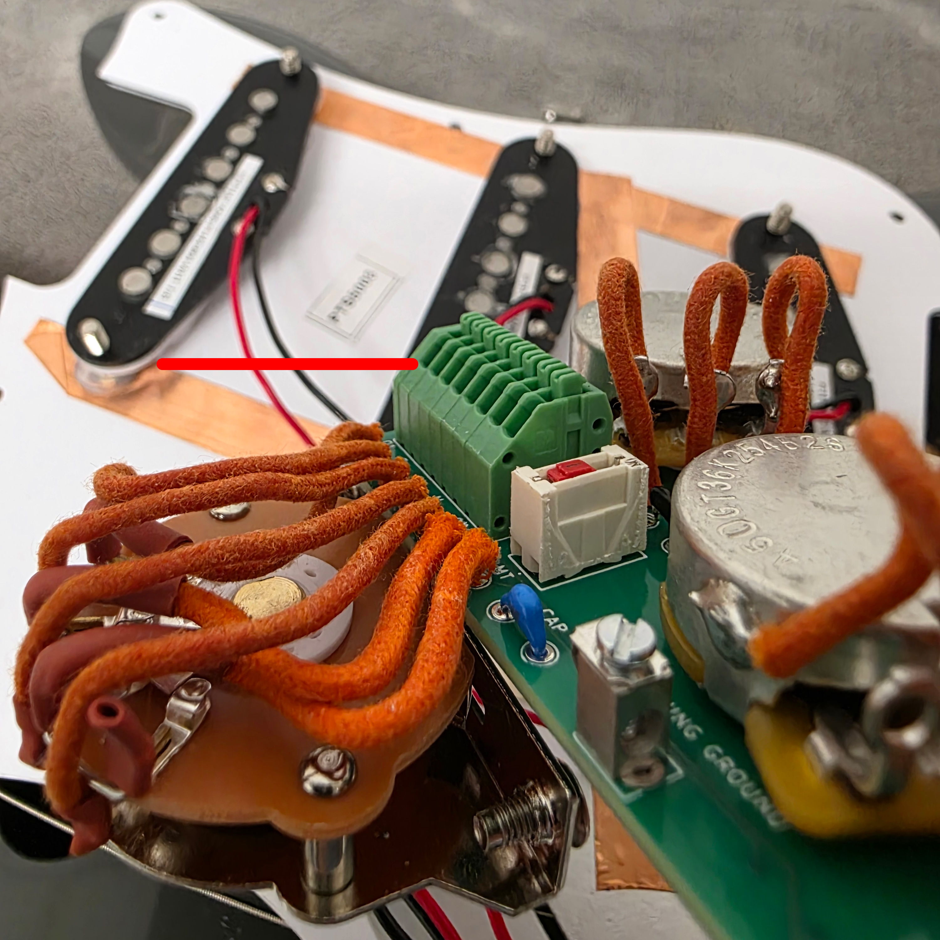 Close-up of guitar wiring and components, showing connections and circuit board details.