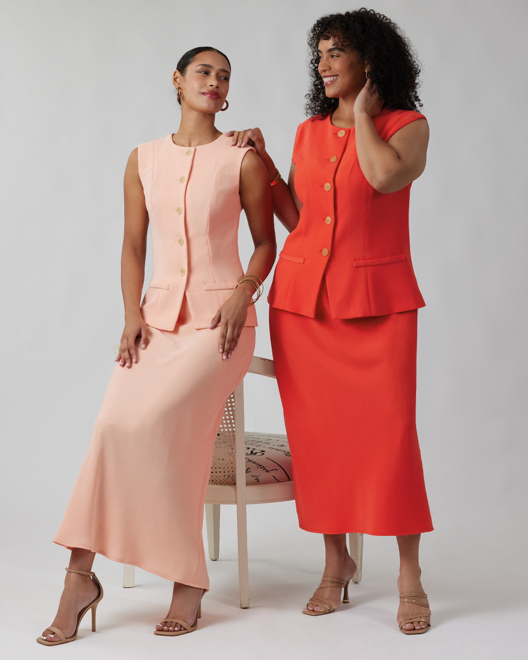 Two women in stylish dresses posing together against a neutral background.