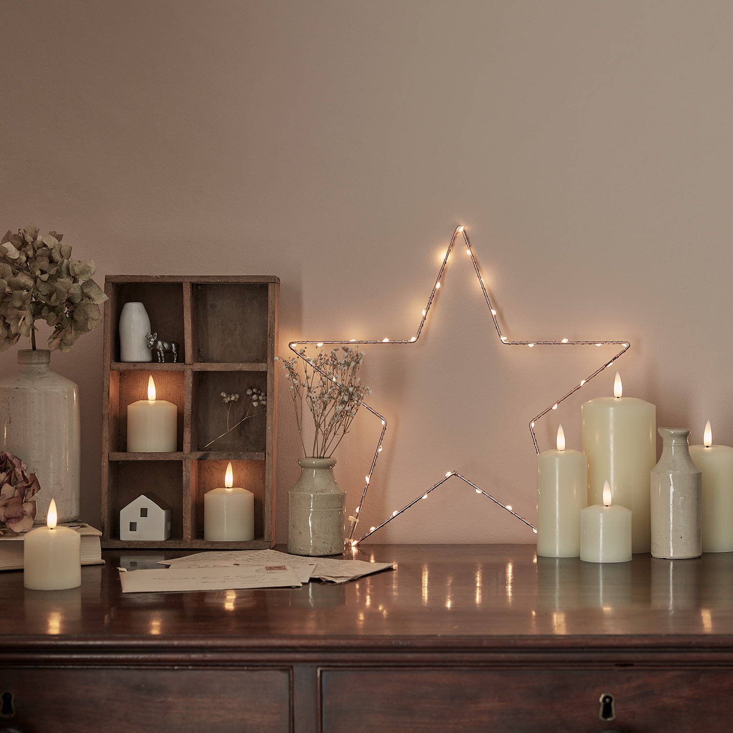 A side table with LED candles, ornaments, an osby star and flowers in a cosy setting.