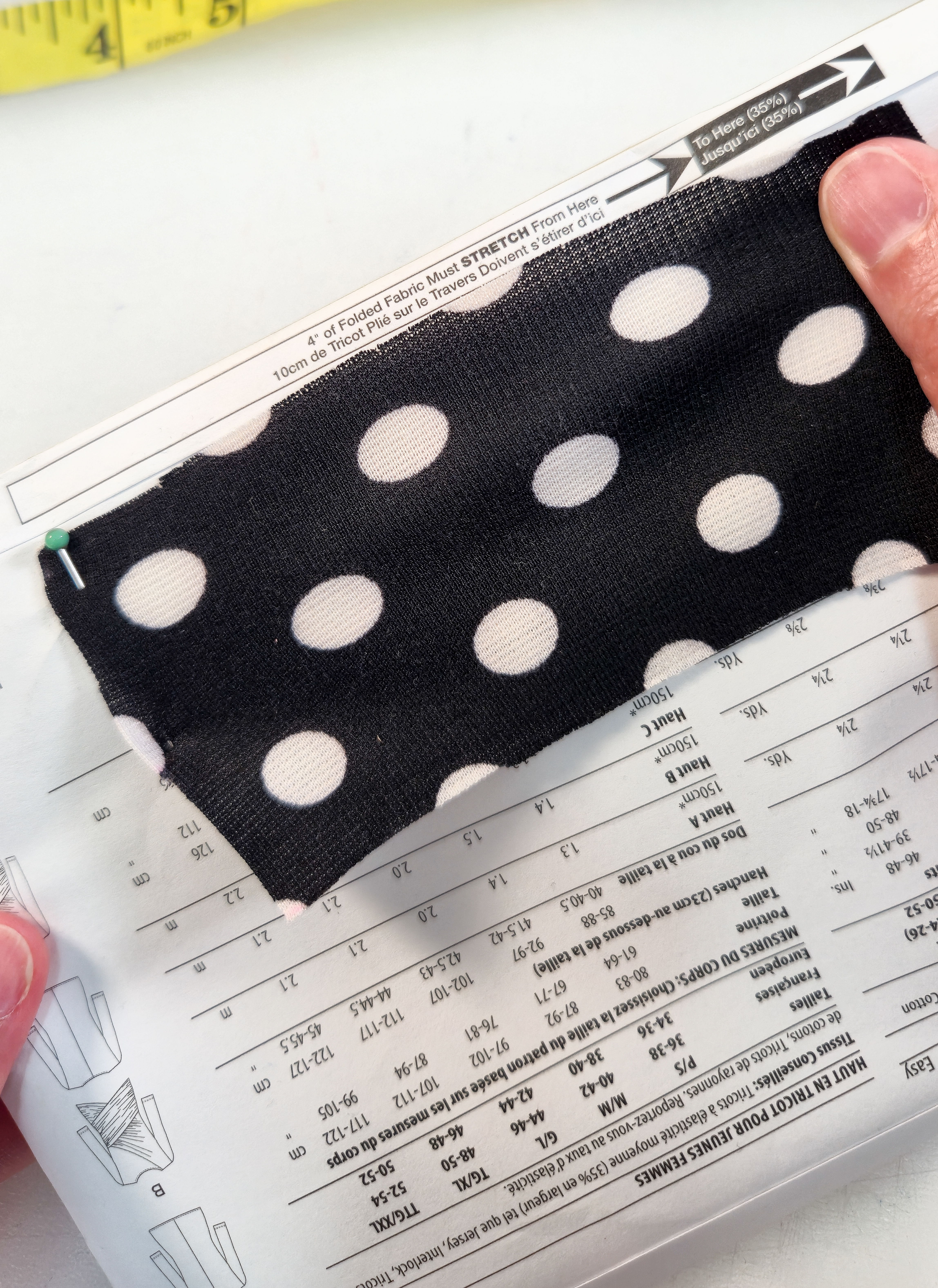 Hands holding a polka dot fabric over a sewing pattern guide.