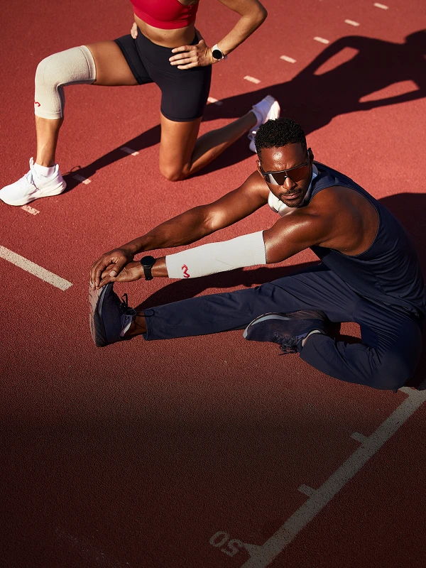 Two athletes stretching on a running track in athletic wear.