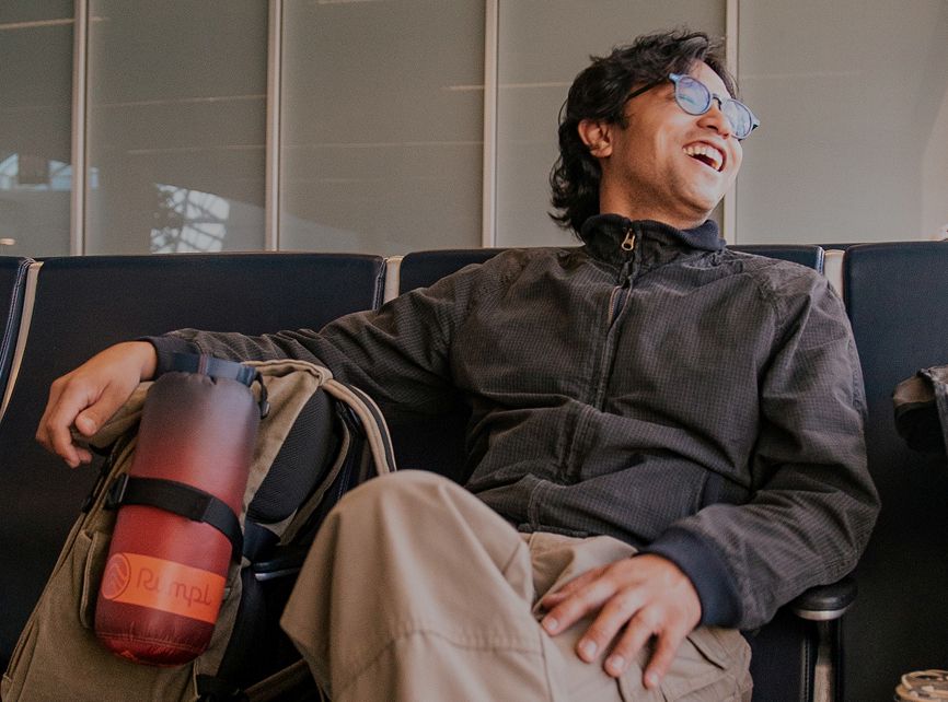 Smiling person sitting with a backpack in a waiting area.