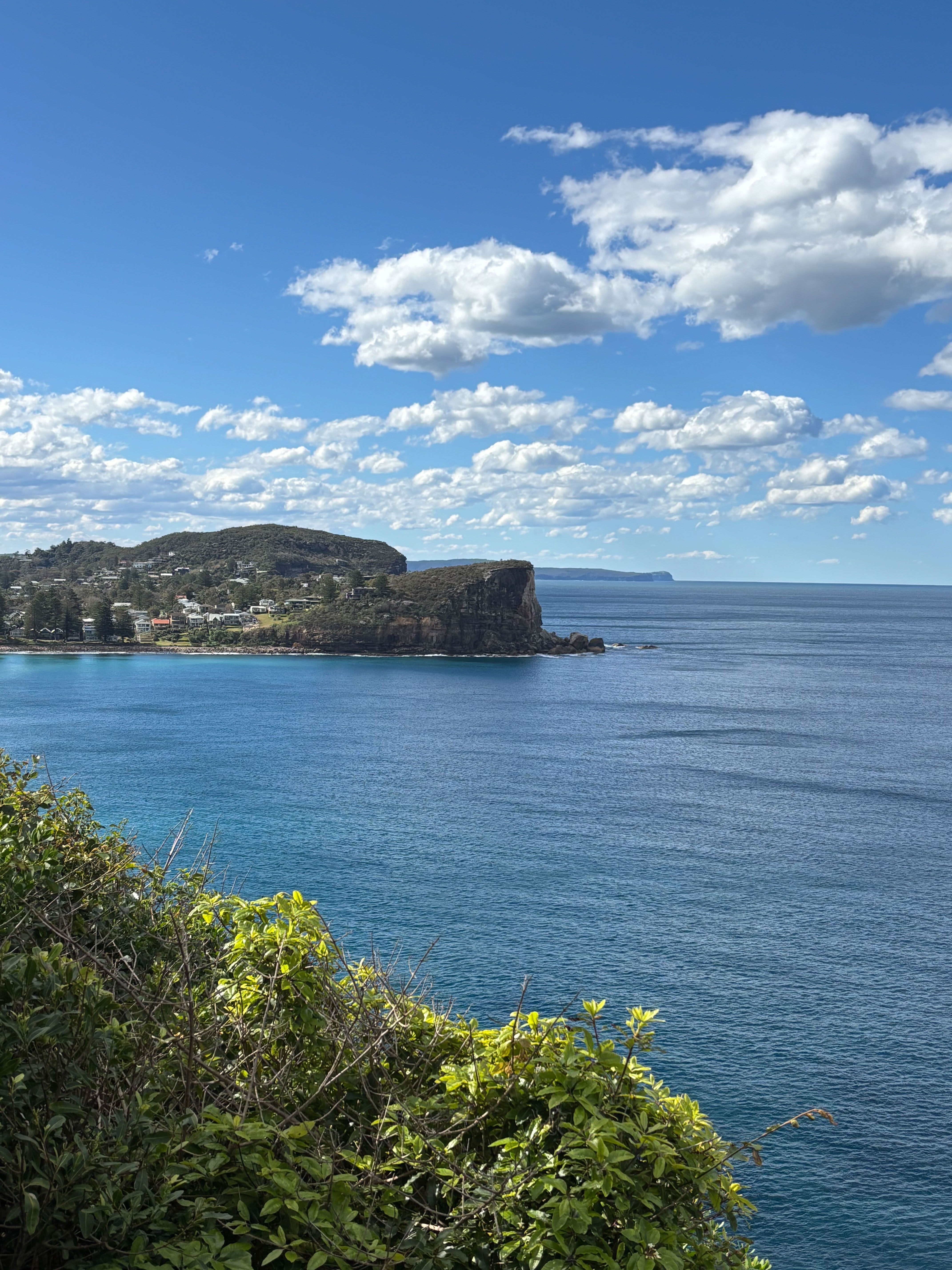Coastal view with blue water, rocky cliffs, and scattered clouds.