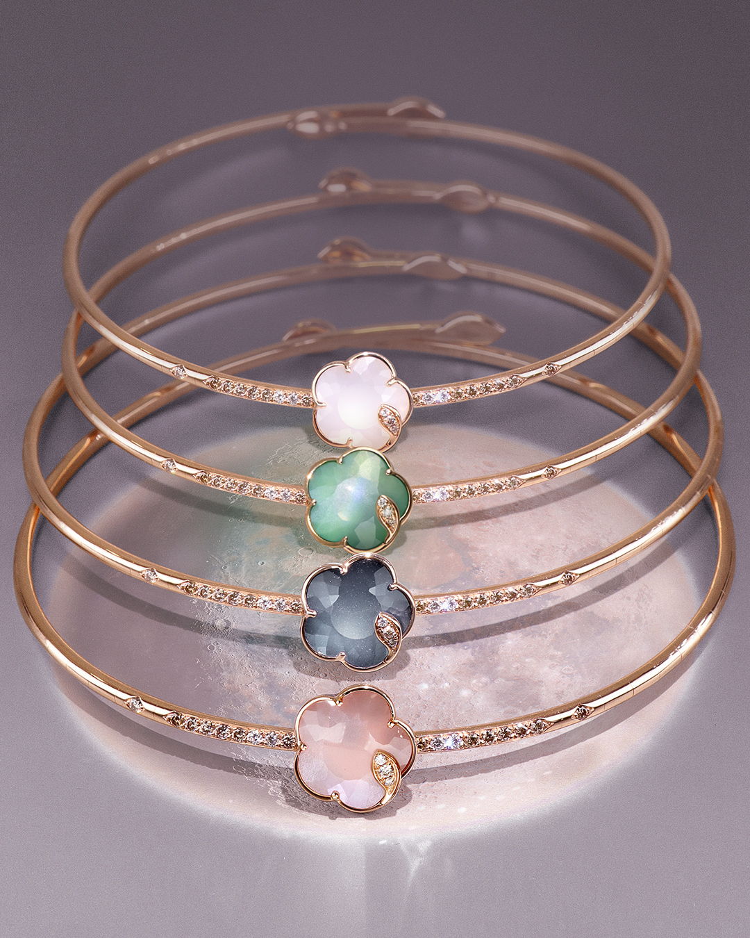 Four gold bangles with colorful flower-shaped accents arranged neatly.