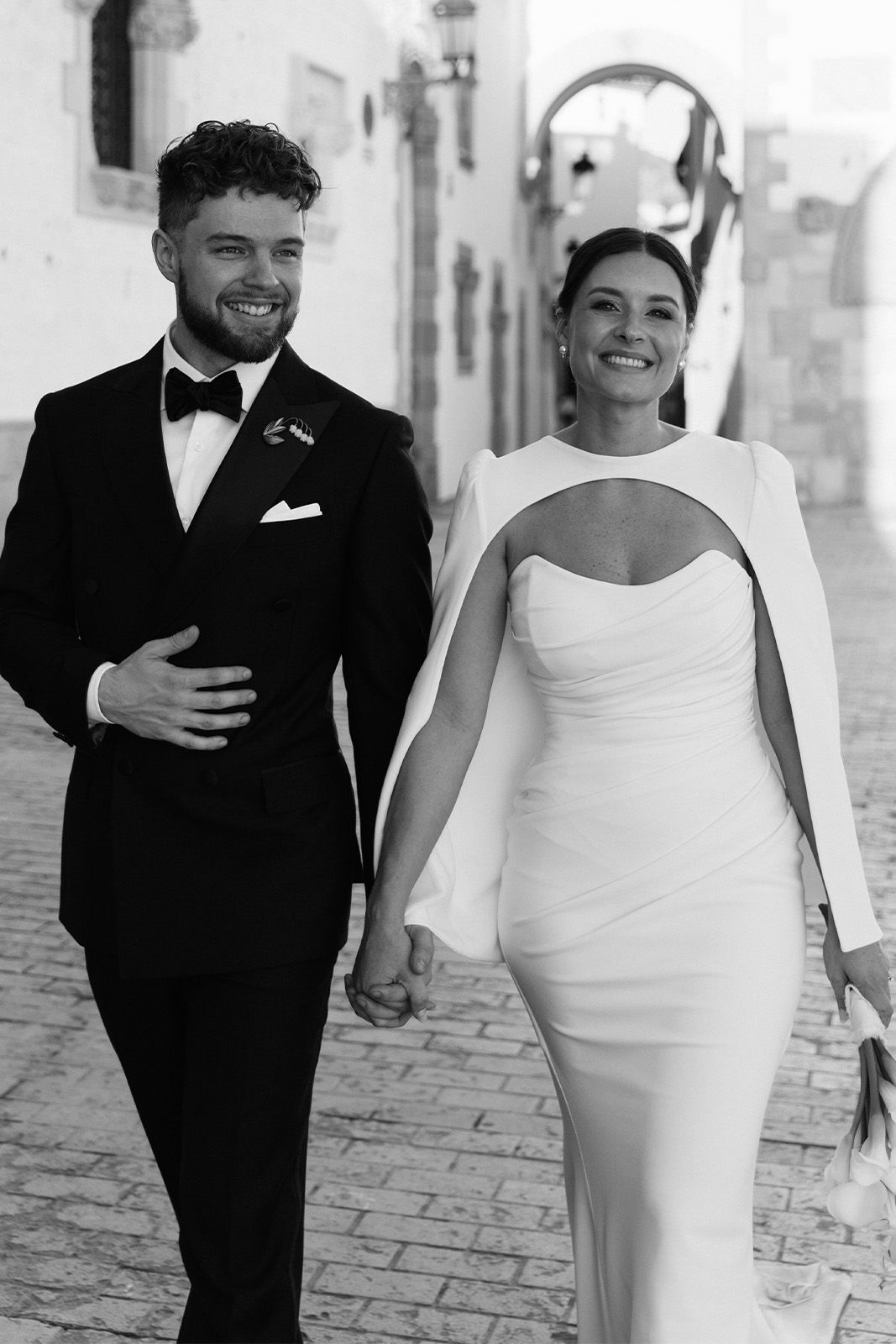 Couple walking hand in hand, dressed elegantly in black and white attire.