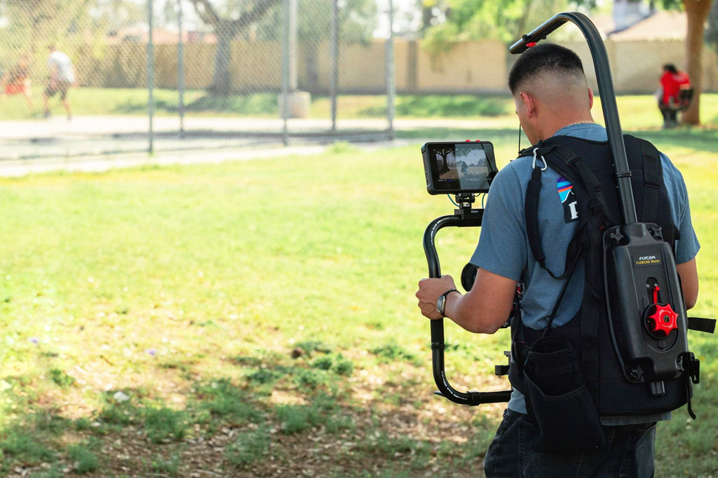 Person with camera equipment walking in a park.