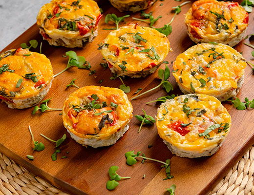 Mini frittatas on a wooden board, garnished with herbs.