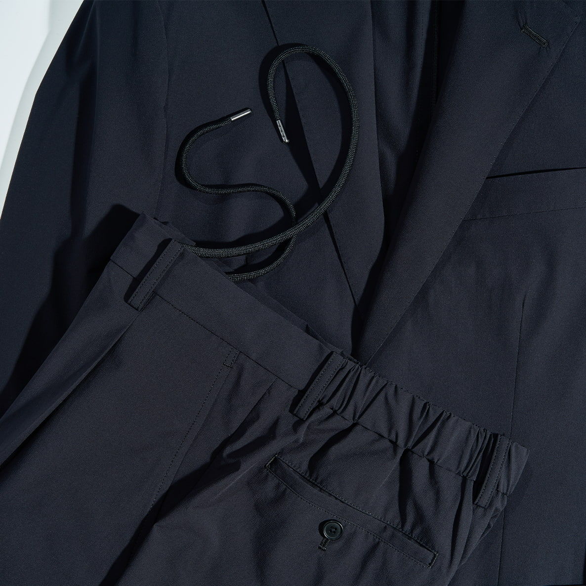 A black suit jacket and matching trousers laid out together.