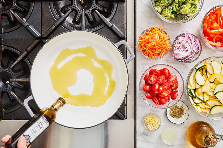 Olive Oil added to pan with ingredients for pasta primavera off to the side