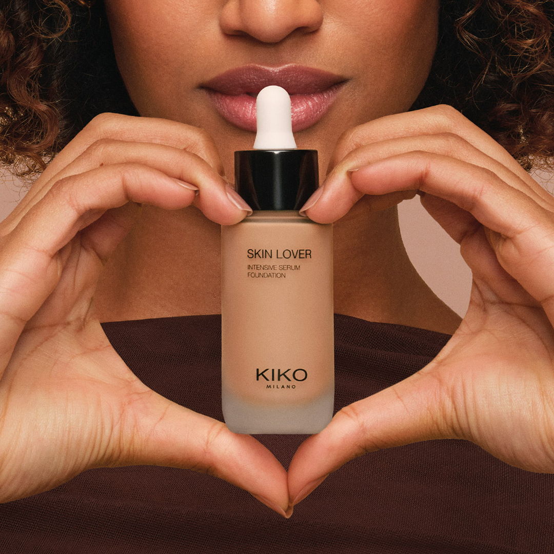 Person holding a bottle of foundation, forming a heart shape with hands.