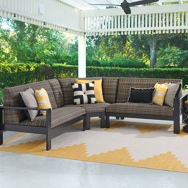 Outdoor seating area with sectional sofa and decorative pillows on a patterned rug.