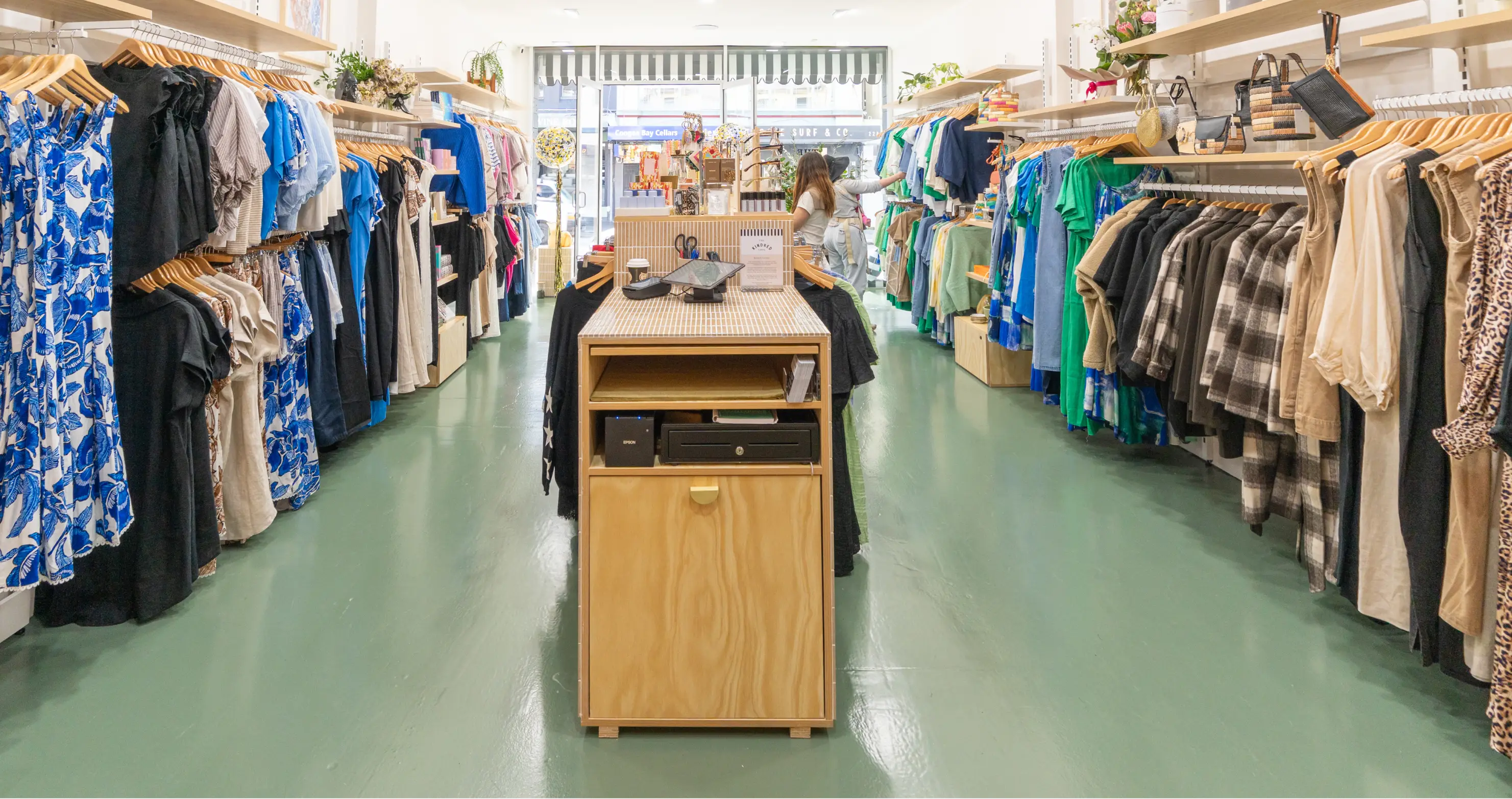 Clothing store aisle with various garments displayed on racks and a checkout counter.