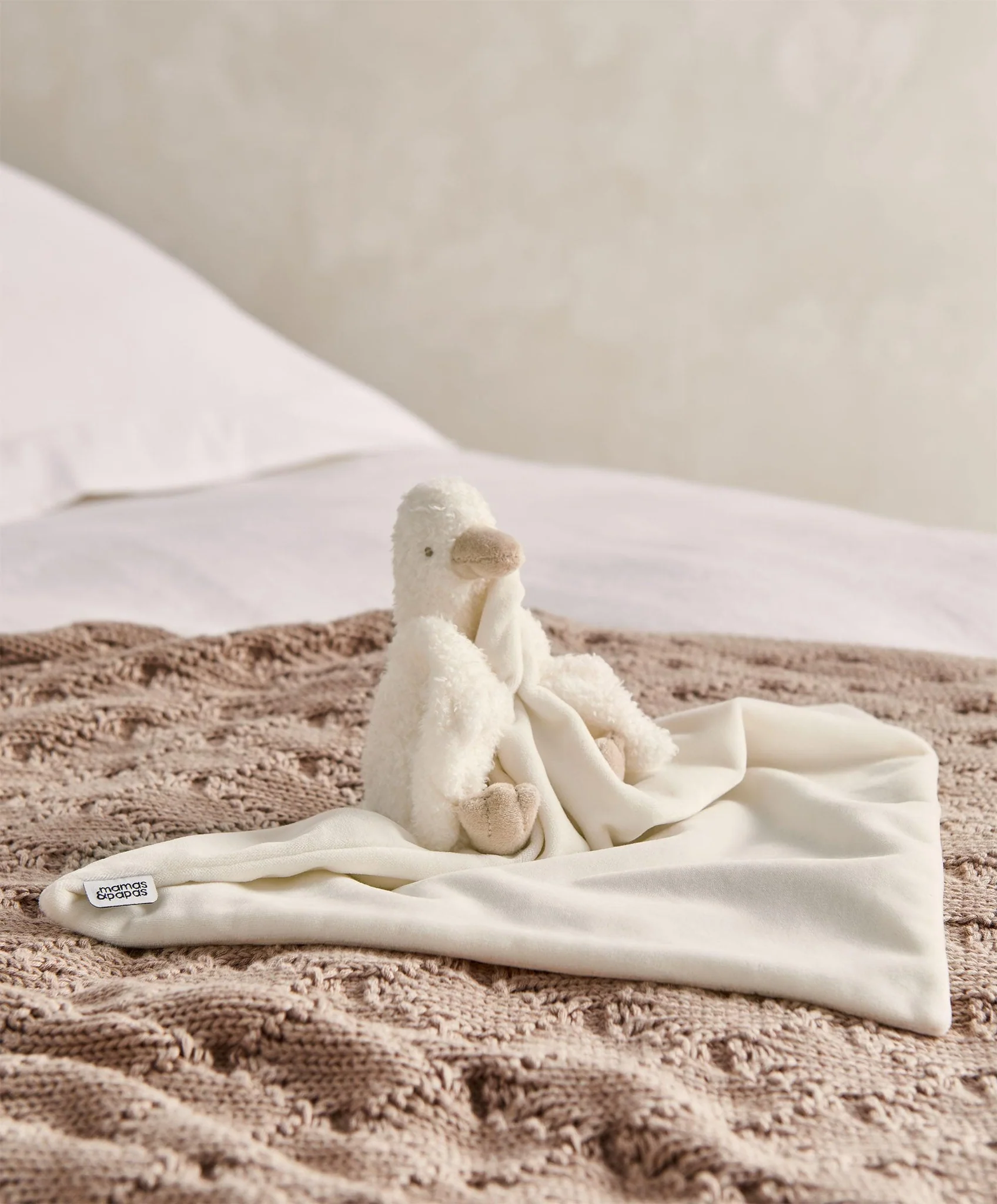 A soft, cream-colored stuffed animal on a cozy blanket.