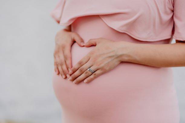 Pregnant Woman Wearing Pink Dress Holding Hands On Stomach