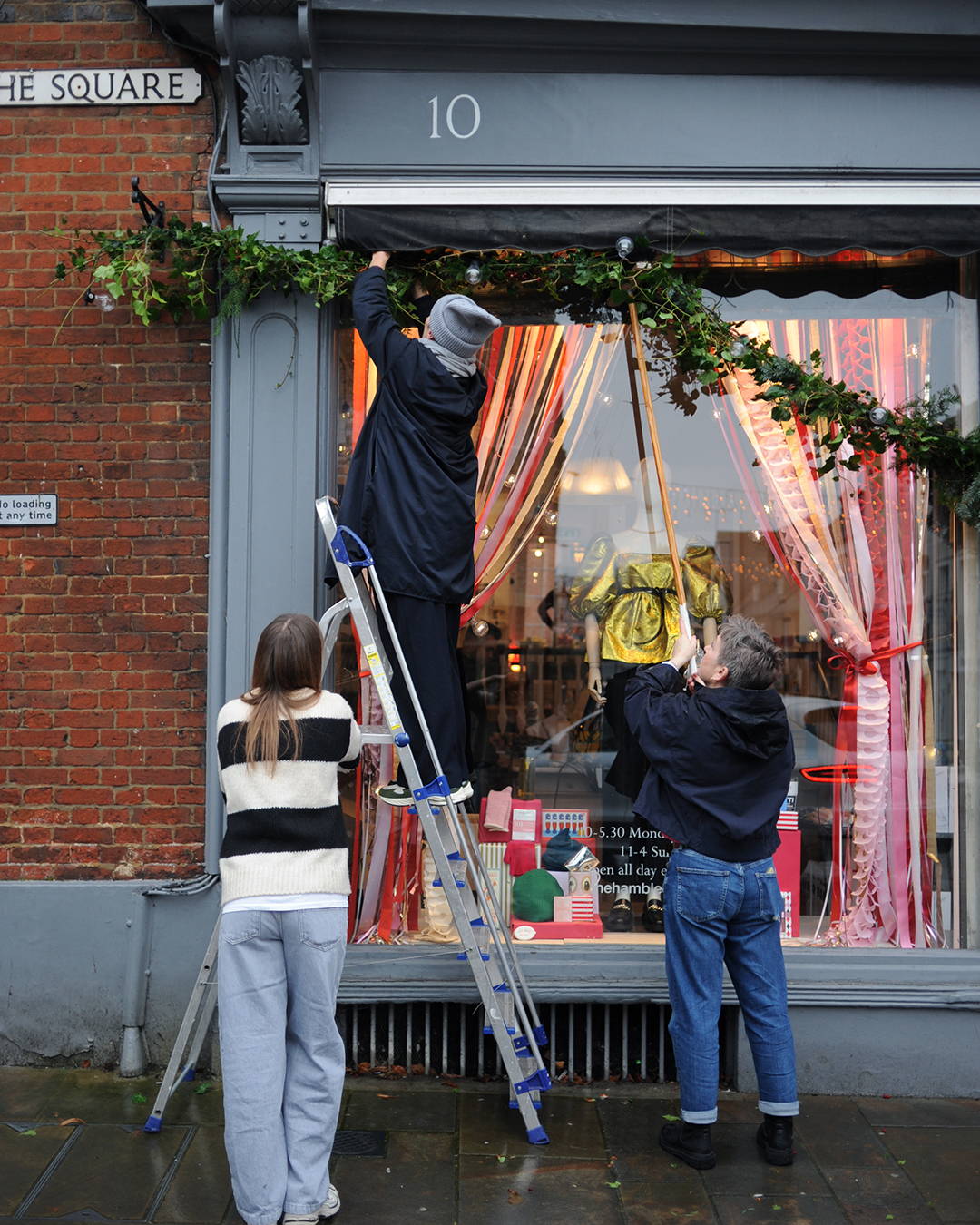 Poppy, Victoria and Katie putting up the annual christmas garland on the shop front.