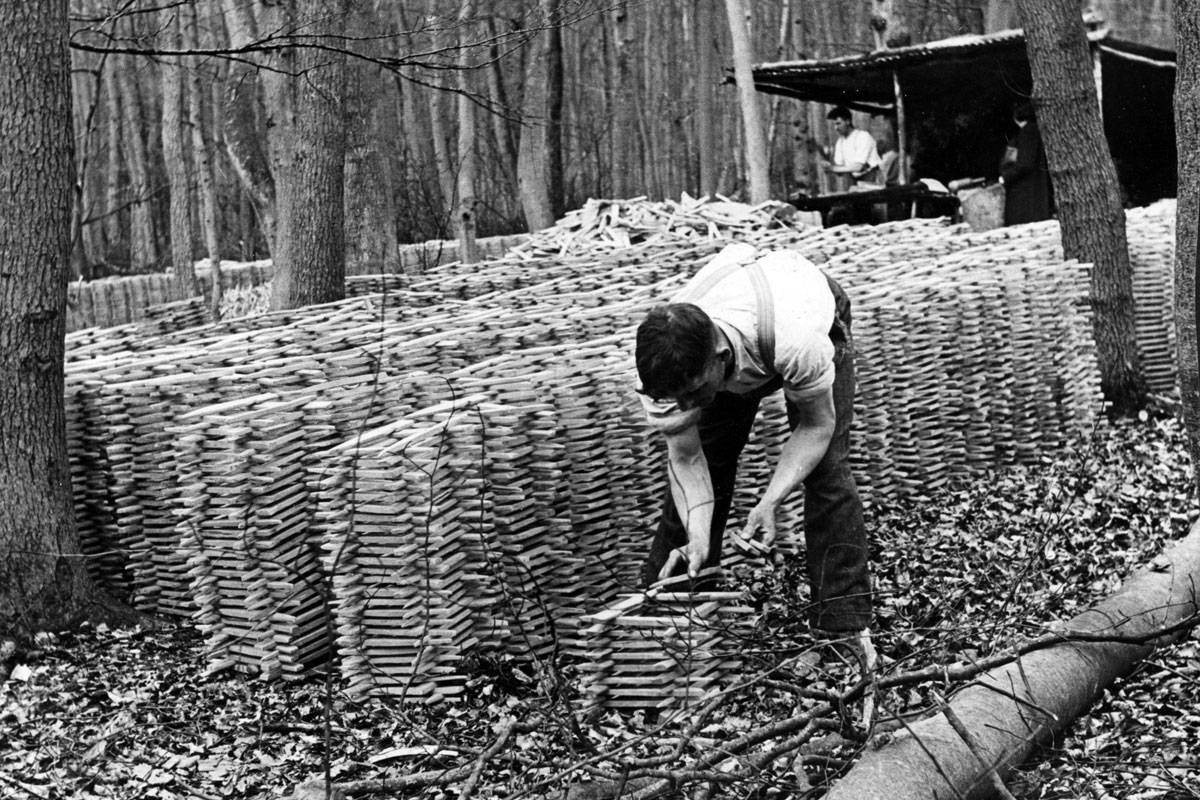 A black and white photo of a man stacking wood pieces in careful piles