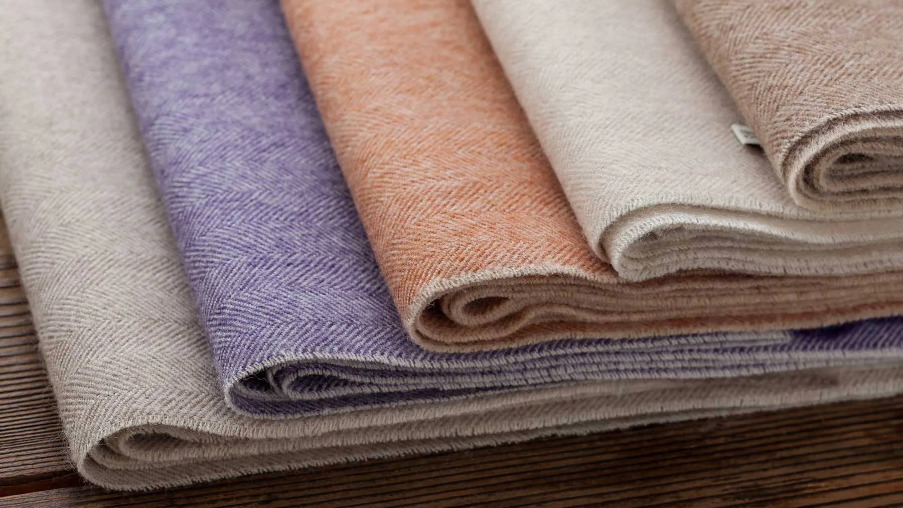 Various rolls of fabric in pastel colors on a wooden surface.