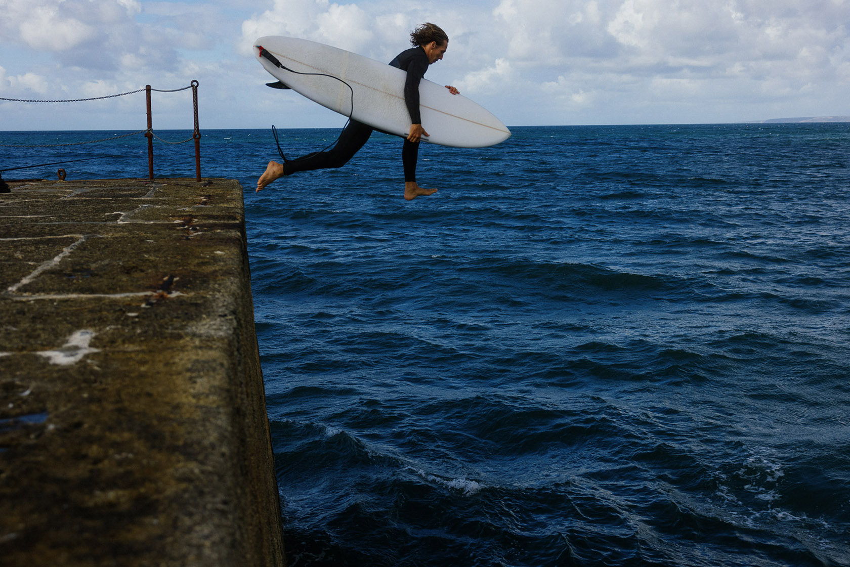 Surfer jumping off a pier into the ocean.