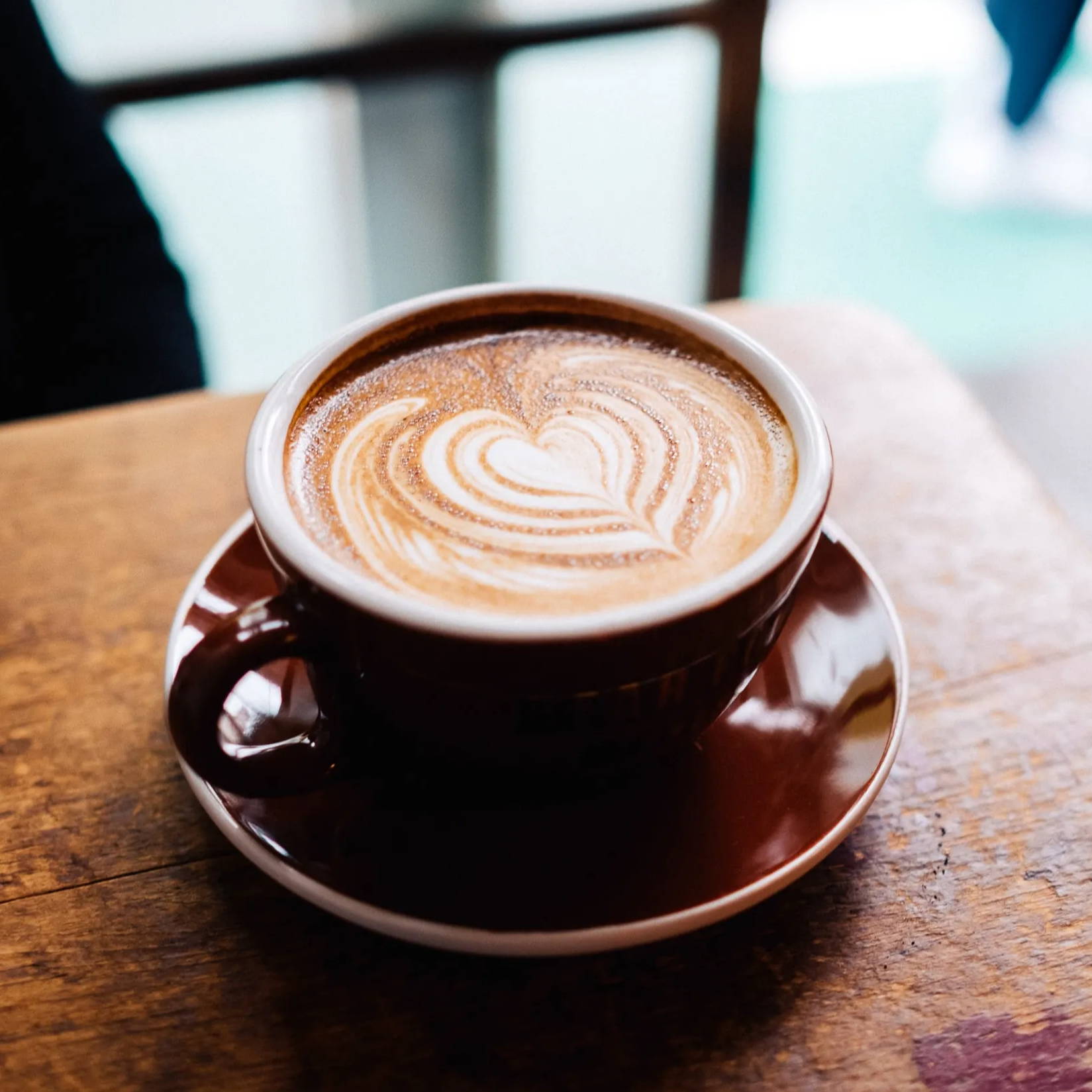 A cup of coffee in a red mug and saucer on a coffee shop table.