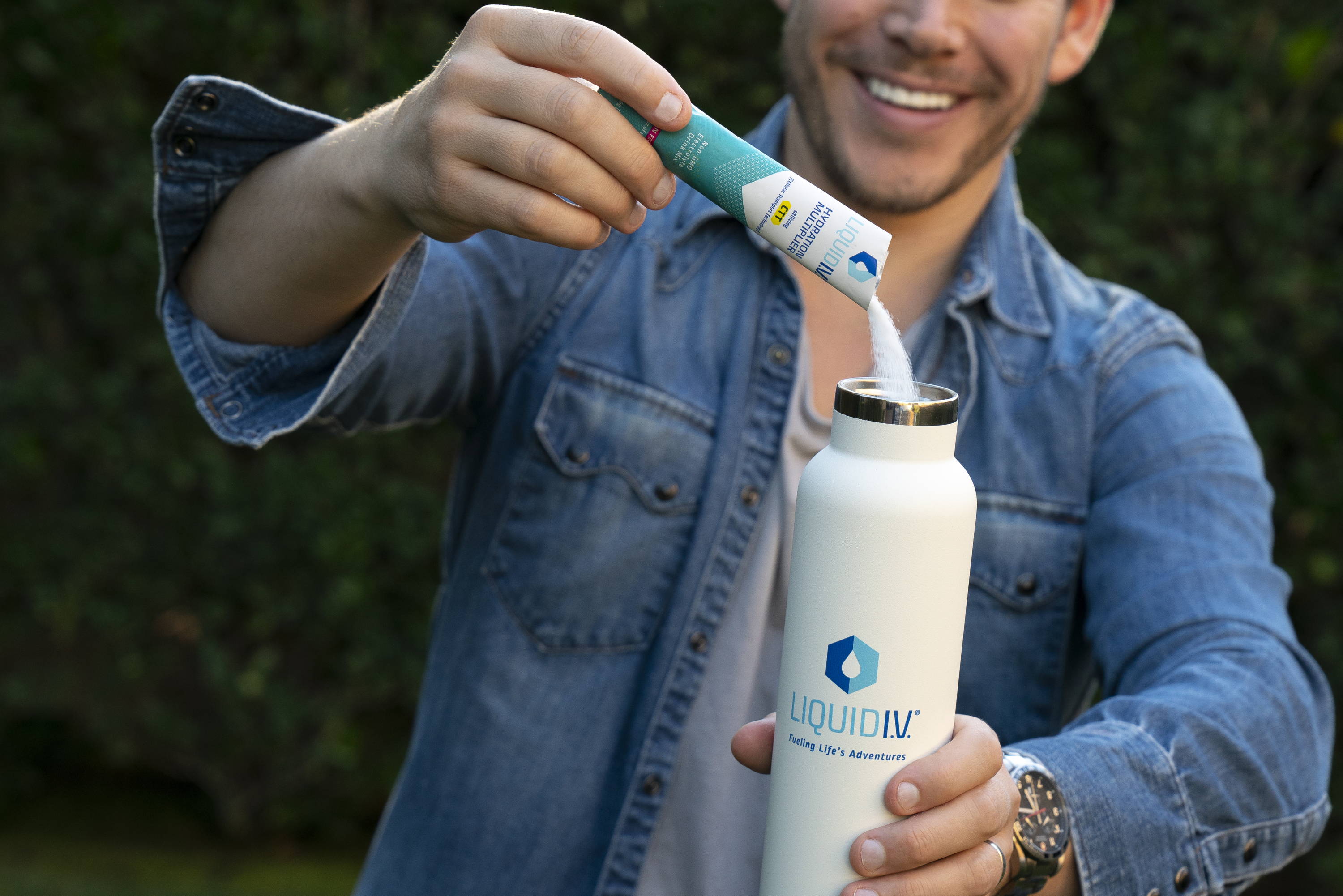 A frequent user of oral rehydration solutions pours Liquid IV's electrolyte powder into a white bottle, smiling in the background.