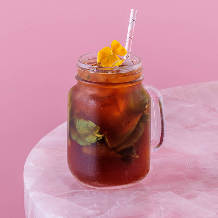Peach iced tea with mint and pink straw on pink background