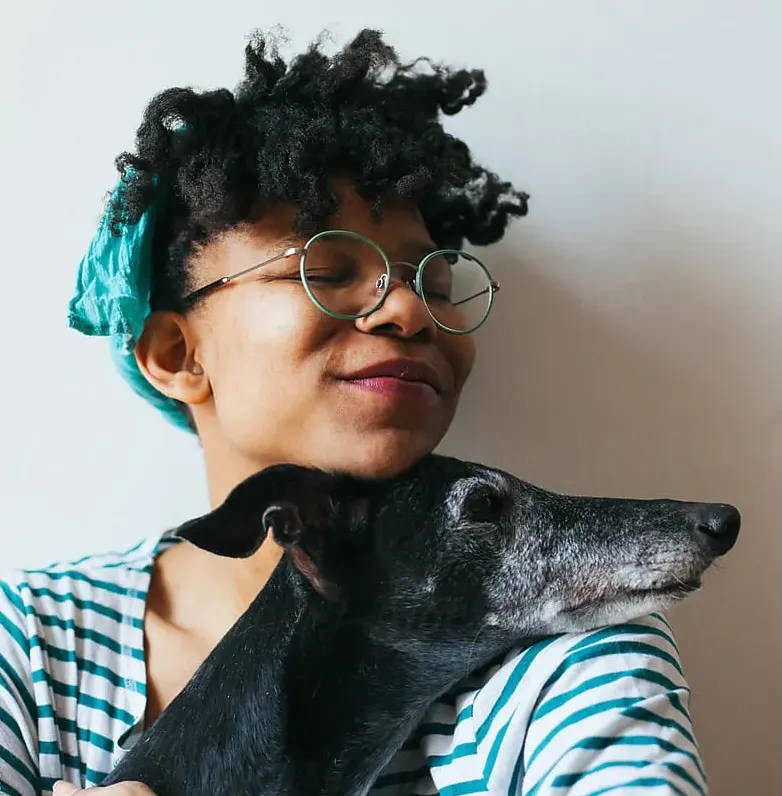 An black women with a hair tie in cuddling with an older grey hound