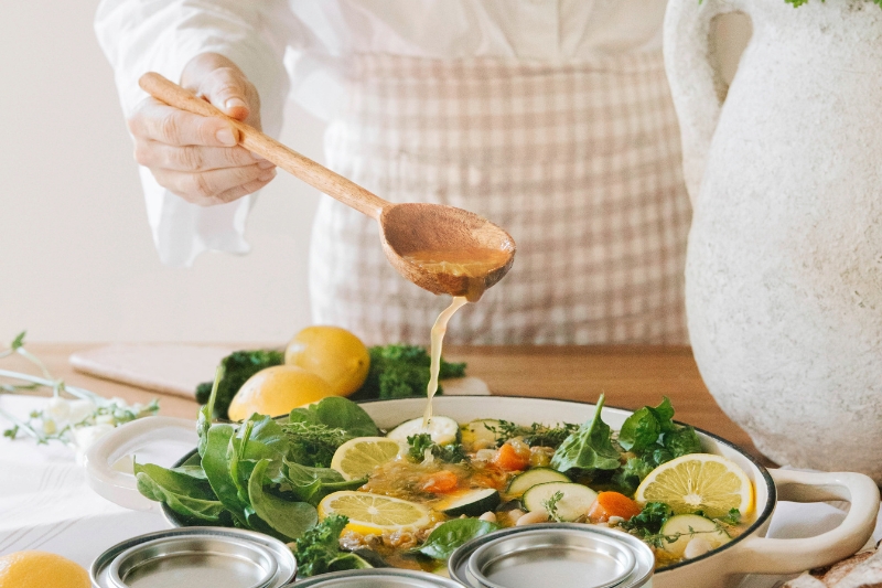 Person serving a vegetable dish with a wooden spoon and fresh lemons.