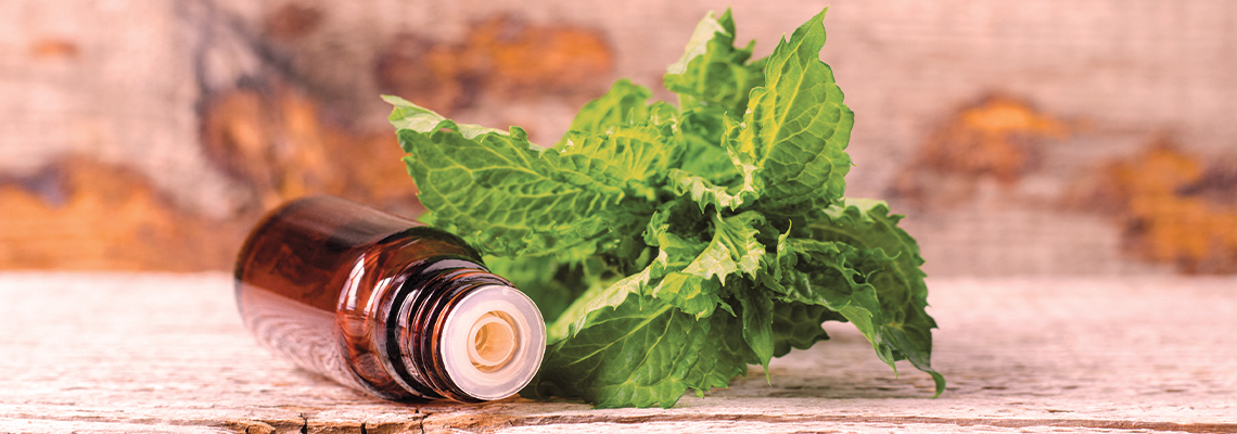 Brown glass bottle beside fresh mint leaves on a wooden surface.