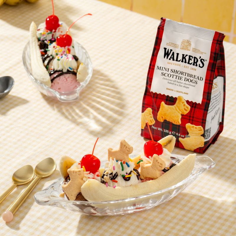 Two ice cream sundaes with cherries and a bag of Walkers biscuits.