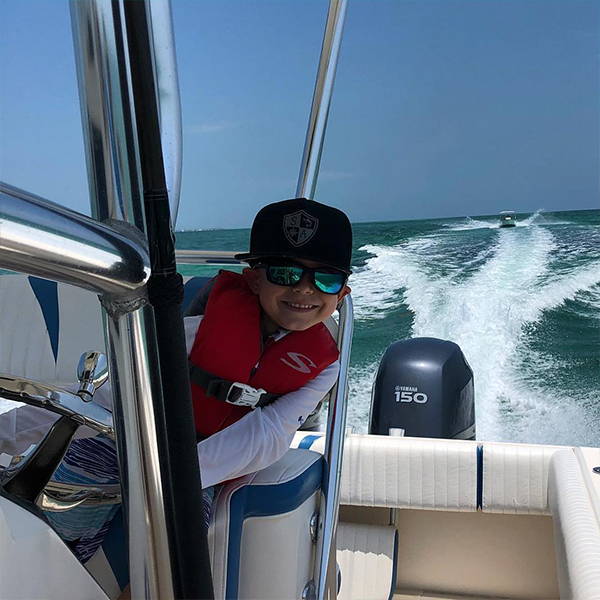 Bosun Lindsey piloting an outboard fishing boat while wearing a black SA Company hat.