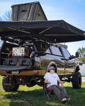 Overland setup on black and bronze Ram truck with rooftop tent, awning, and bronze train horns visible underneath