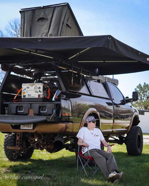 Overland setup on black and bronze Ram truck with rooftop tent, awning, and bronze train horns visible underneath