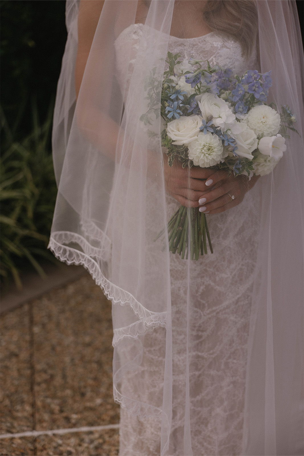 Bride holding a bouquet, wearing a lace wedding dress and veil.