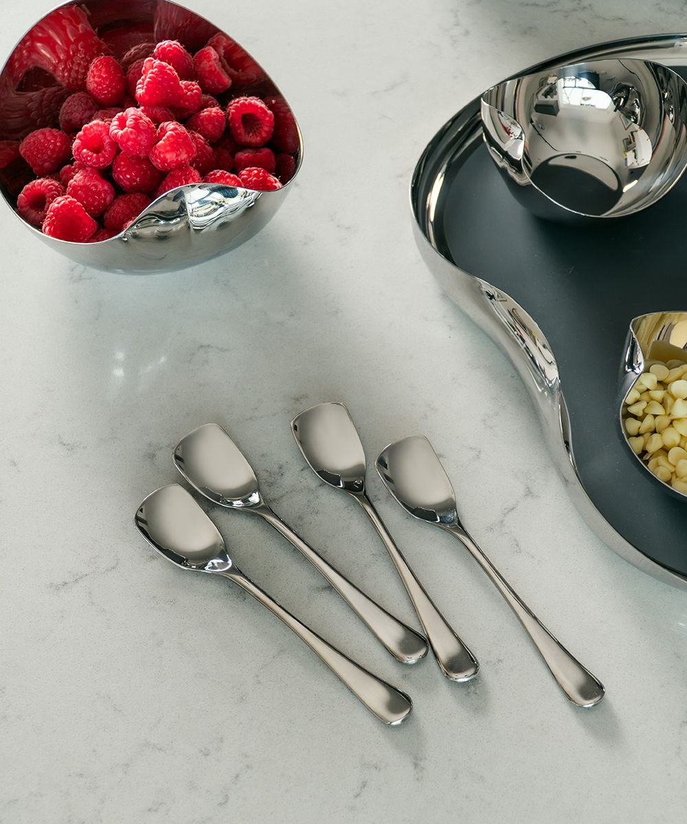 Ice cream spoons next to Drift bowls of raspberries and white chocolate on a countertop.