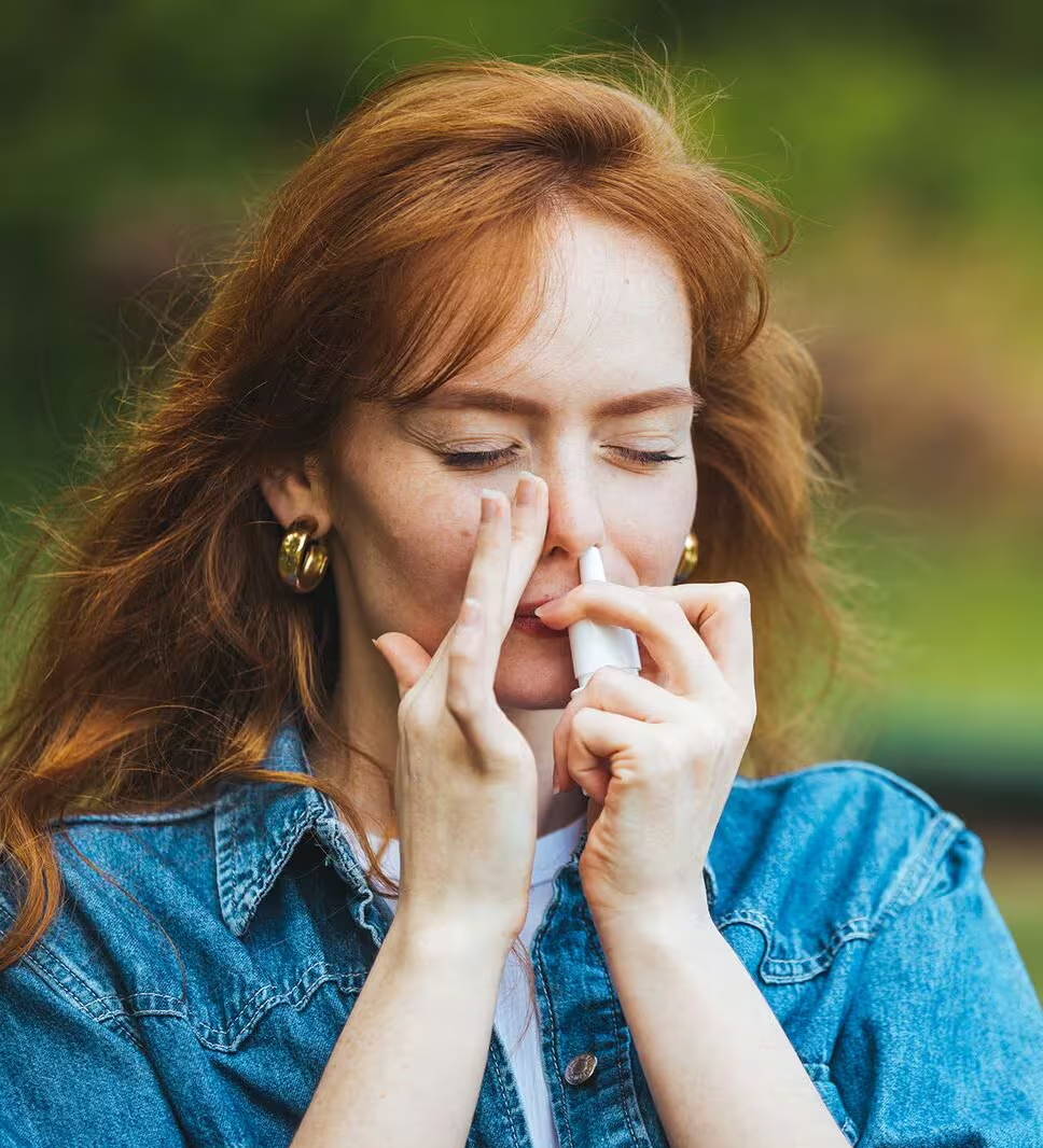 Žena používa nosový sprej na alergickú nádchu, počas toho ako je vonku - vysoká koncentrácia peľu u nej vyvoláva príznaky alergie