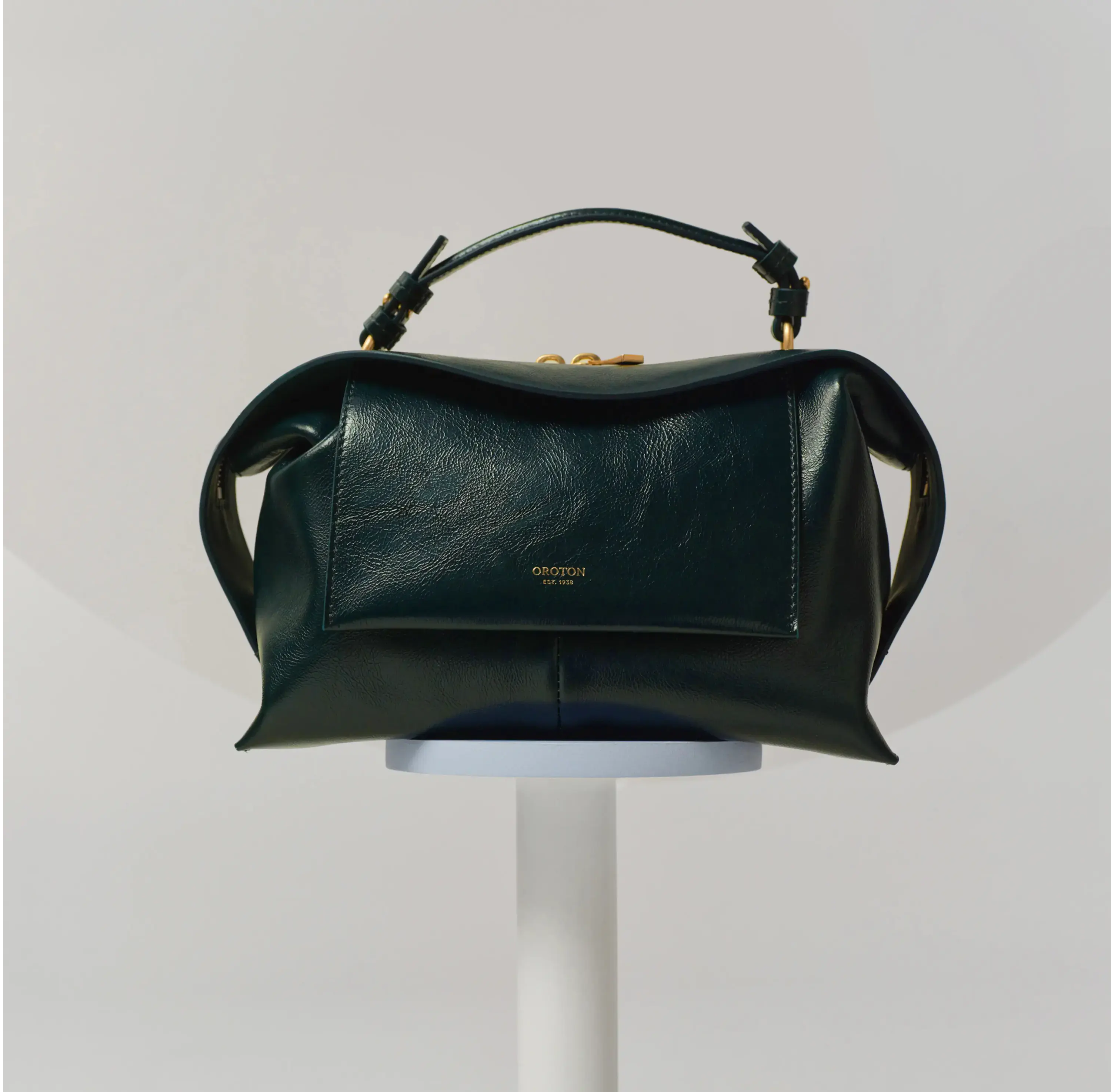 A green leather handbag displayed on a pedestal against a neutral background.