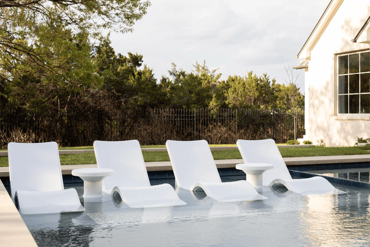 White in-pool lounge chairs and side table on a tanning ledge for resort style poolside design.