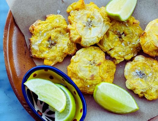 Fried plantains served with lime wedges on a wooden plate.
