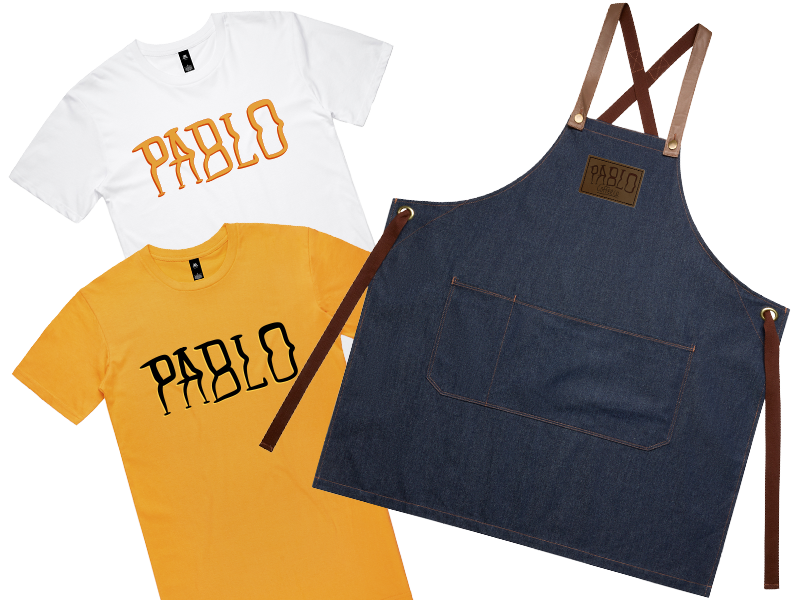 Pablo coffee co uniform items including gold tee and denim apron with leather patch