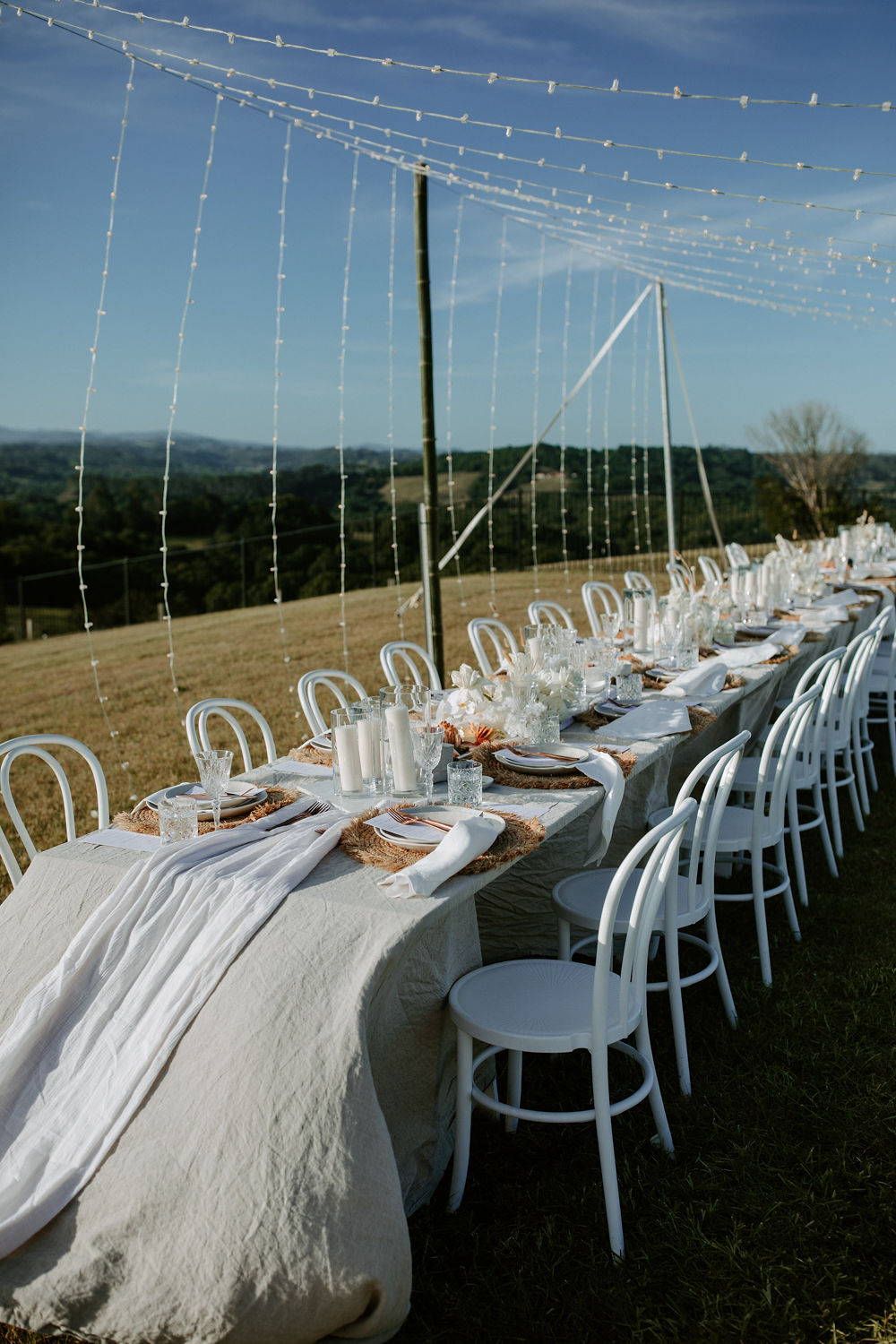 Long outdoor dining table for wedding reception with white chairs