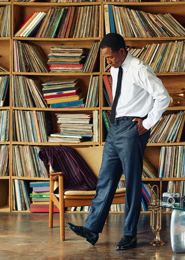 Man in formal wear standing near a bookshelf filled with vinyl records.